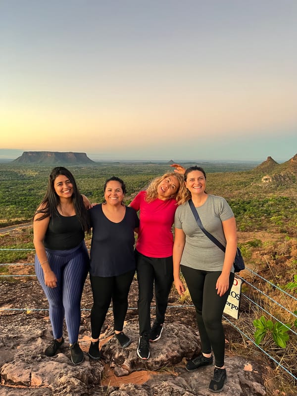 Quatro mulheres abraçadas no mirante do Portal ao entardecer, com as mesas no horizonte